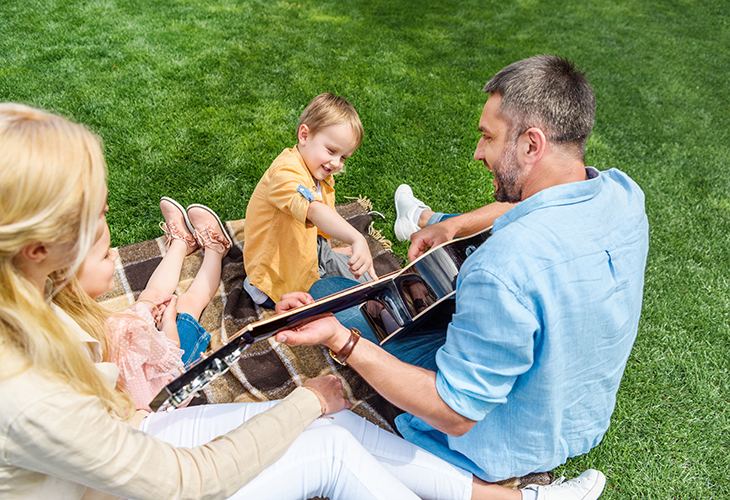 A dad playing guitar outside for his two young children and their mom.